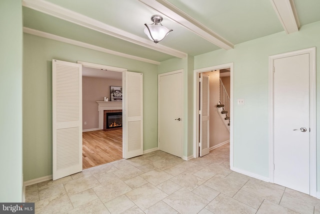 unfurnished room with a glass covered fireplace, stairs, beam ceiling, and baseboards