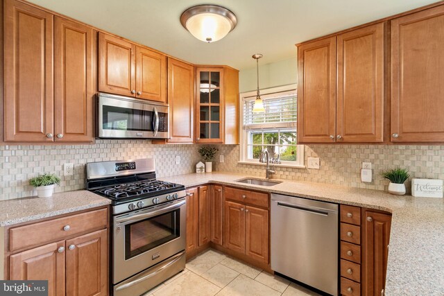 kitchen featuring appliances with stainless steel finishes, a sink, light stone counters, and decorative backsplash