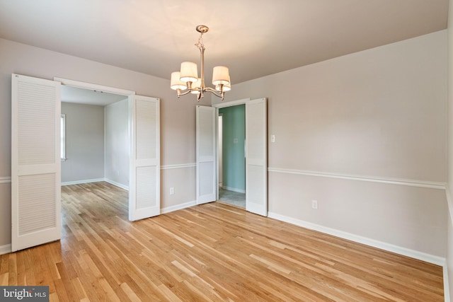 spare room with a chandelier, light wood-style flooring, and baseboards