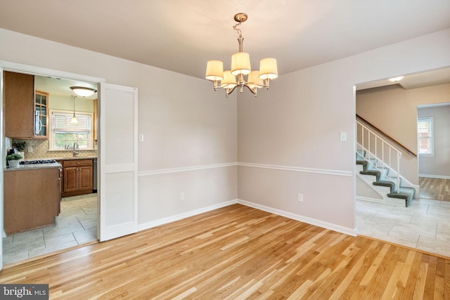 unfurnished dining area featuring light wood finished floors, a chandelier, plenty of natural light, and baseboards