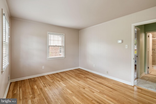 empty room featuring light wood finished floors, crown molding, and baseboards