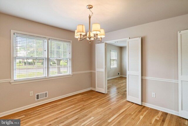 spare room with a chandelier, baseboards, and light wood finished floors