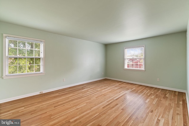 unfurnished room with healthy amount of natural light, light wood finished floors, and baseboards