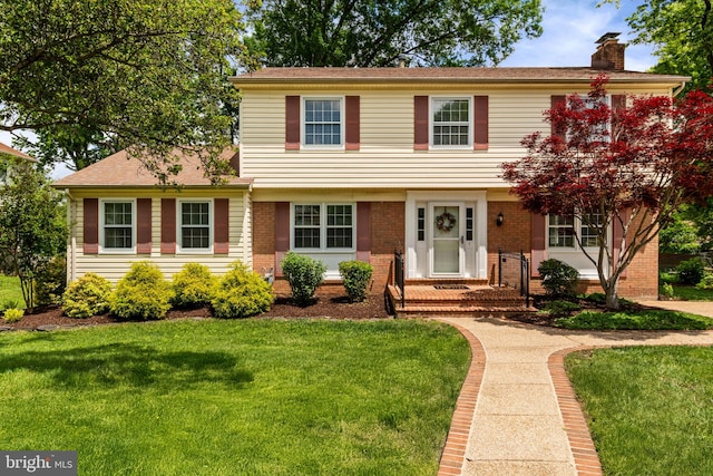 colonial home featuring a chimney, a front yard, and brick siding