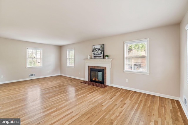 unfurnished living room with light wood-style flooring, healthy amount of natural light, a brick fireplace, and baseboards