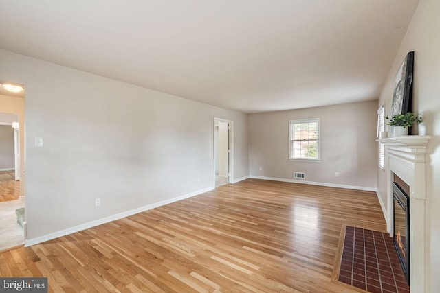 unfurnished living room with a fireplace with flush hearth, light wood-style flooring, and baseboards