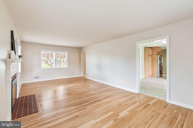 unfurnished living room featuring light wood finished floors, a tile fireplace, and baseboards