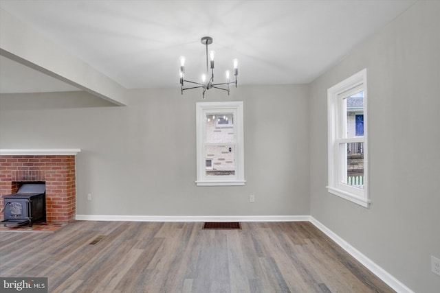 unfurnished living room featuring a chandelier, wood finished floors, a wood stove, and baseboards