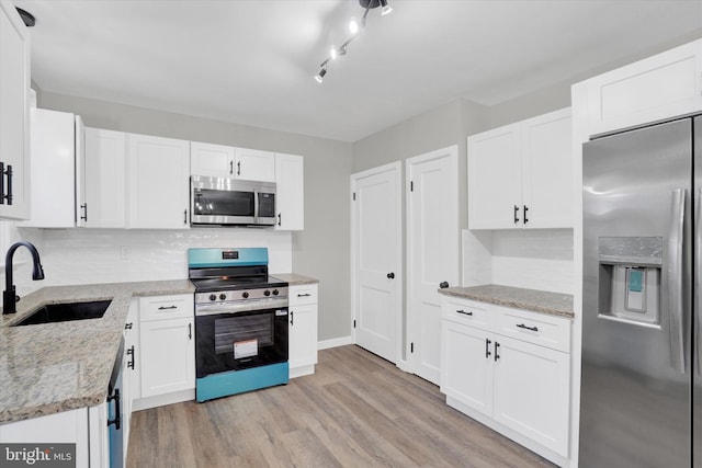 kitchen with appliances with stainless steel finishes, a sink, decorative backsplash, and light wood-style floors
