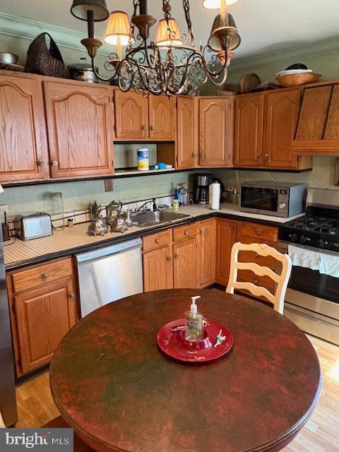kitchen featuring appliances with stainless steel finishes, light wood finished floors, a sink, a chandelier, and crown molding