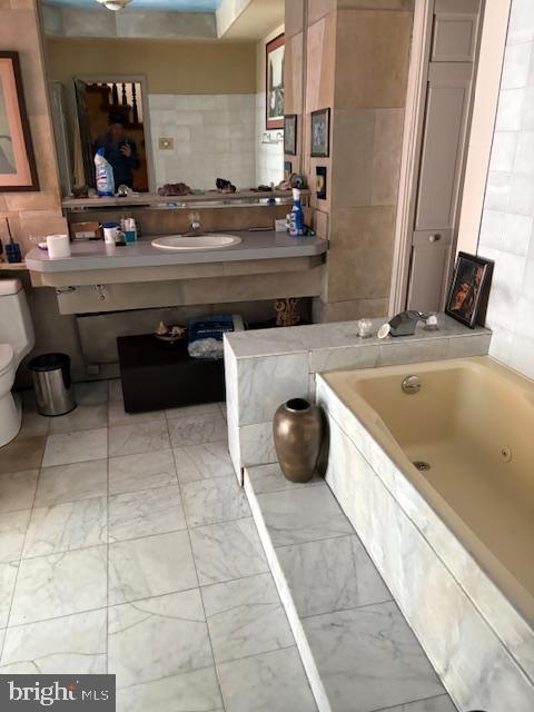 full bathroom with a jetted tub, marble look tiles, toilet, and a sink