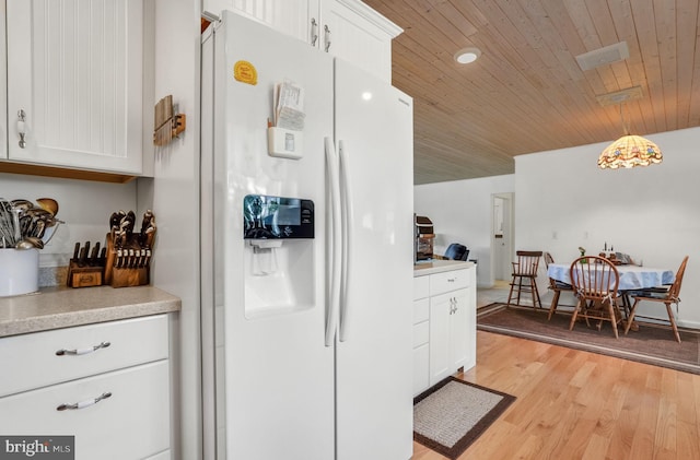 7466 Beebe Rd, Chincoteague Island, VA 23336 - kitchen with white refrigerator with ice dispenser, white cabinetry, light countertops, light wood-style floors, and hanging light fixtures