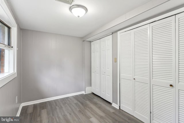 unfurnished bedroom featuring wood finished floors, baseboards, and two closets