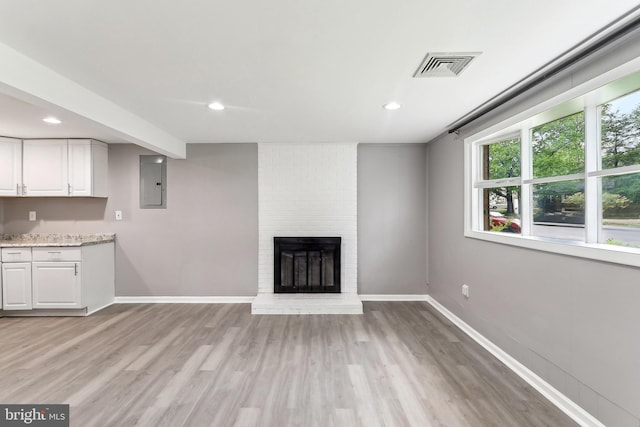 unfurnished living room with light wood-type flooring, baseboards, a fireplace, electric panel, and recessed lighting