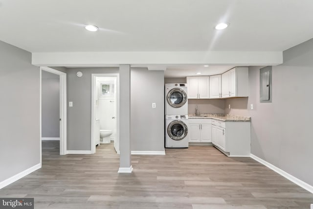 laundry area featuring stacked washer / drying machine, baseboards, electric panel, and recessed lighting