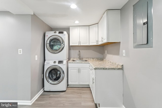 laundry area with electric panel, estacked washer and dryer, light wood-style floors, cabinet space, and baseboards
