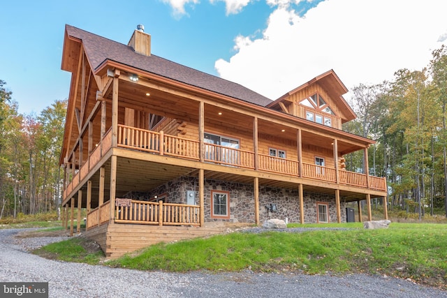 back of property with a chimney, stone siding, a wooden deck, and a shingled roof