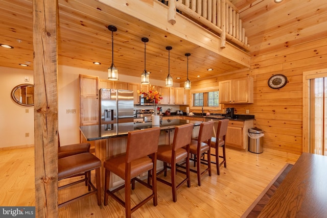 kitchen featuring stainless steel appliances, dark countertops, light wood-style flooring, a breakfast bar, and light brown cabinets