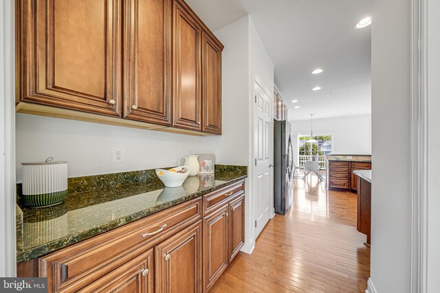 8217 Castanea Ln, Derwood, MD 20855 - kitchen featuring brown cabinetry, freestanding refrigerator, light wood-style flooring, dark stone countertops, and recessed lighting