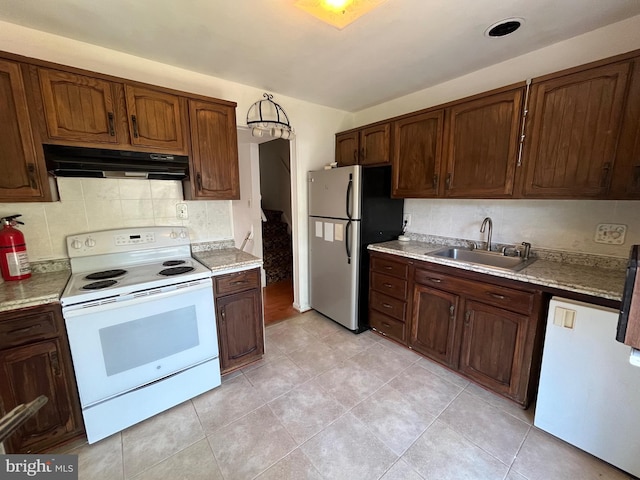 kitchen with white appliances, under cabinet range hood, a sink, and decorative backsplash