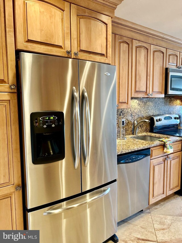 kitchen with stainless steel appliances, light stone counters, a sink, tasteful backsplash, and brown cabinetry