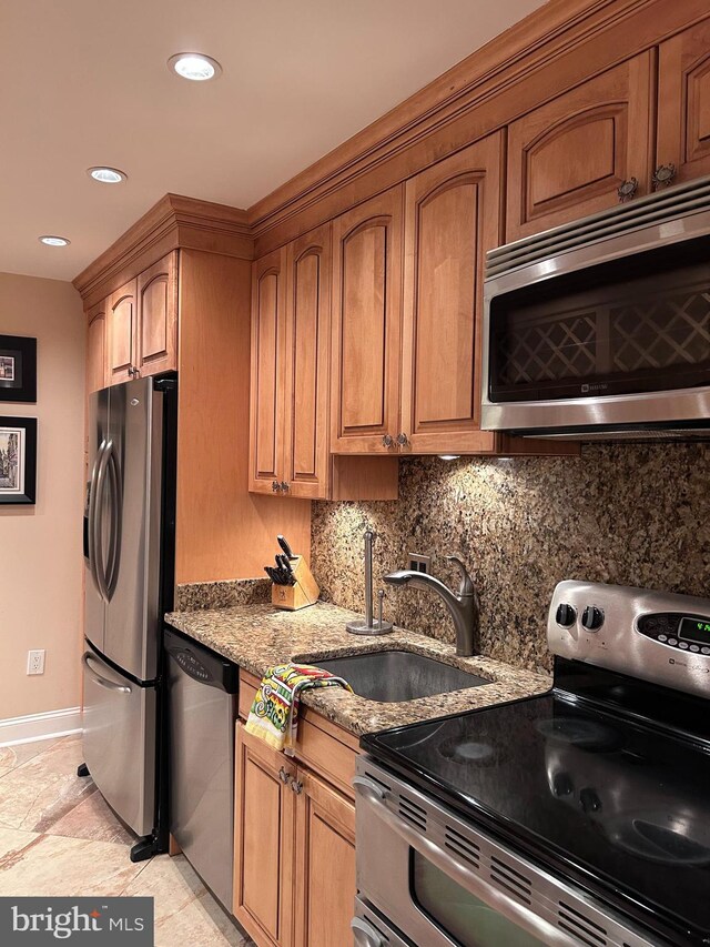 kitchen with stainless steel appliances, a sink, light stone counters, baseboards, and brown cabinets