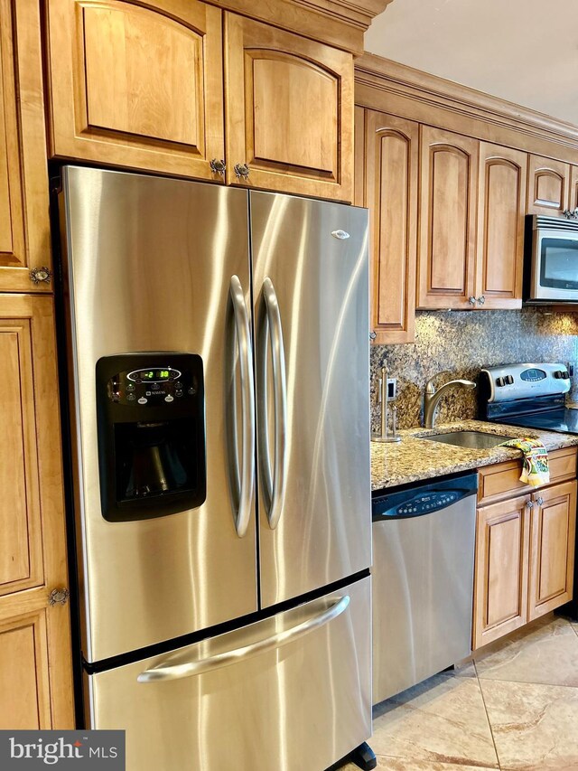 kitchen featuring appliances with stainless steel finishes, light stone countertops, a sink, backsplash, and brown cabinetry