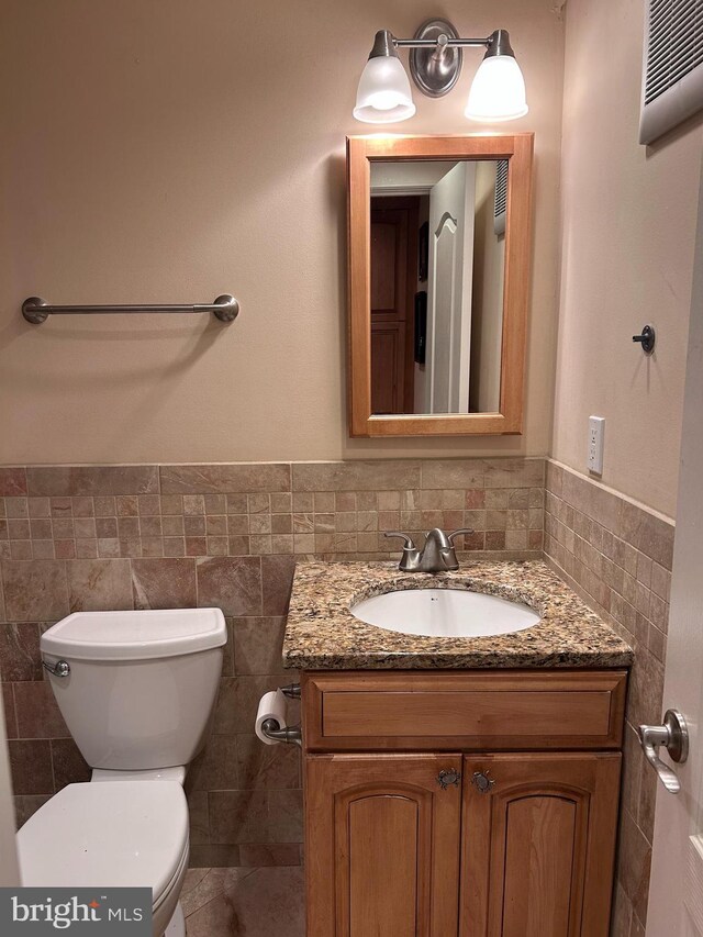 half bath featuring tile walls, toilet, vanity, and a wainscoted wall