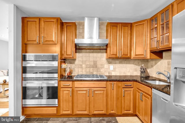 kitchen with appliances with stainless steel finishes, wall chimney range hood, a sink, and dark stone counters