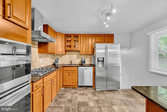 kitchen featuring stainless steel appliances, wall chimney exhaust hood, a sink, glass insert cabinets, and backsplash