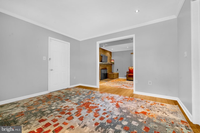 empty room with a brick fireplace, crown molding, wood finished floors, baseboards, and recessed lighting