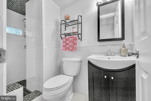 full bath featuring tiled shower, toilet, vanity, tile walls, and a wainscoted wall