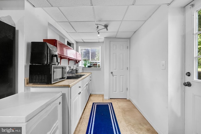 kitchen featuring a paneled ceiling, a sink, light countertops, white cabinetry, and light tile patterned floors