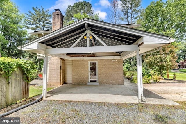 back of house featuring brick siding, a chimney, a patio area, and a detached carport