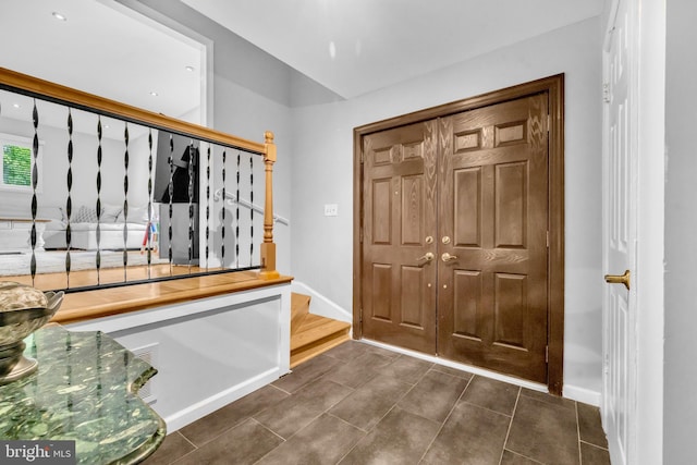 foyer entrance with dark tile patterned flooring, baseboards, and stairs