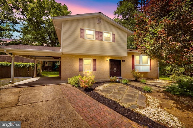 view of front of house with brick siding, a carport, fence, and driveway