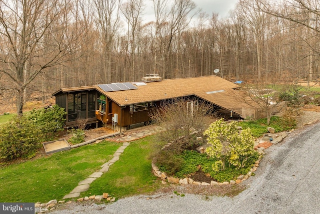 1220 Morgantown Rd, Morgantown, PA 19543 - view of front of property featuring a sunroom, roof mounted solar panels, a front yard, a chimney, and a wooded view
