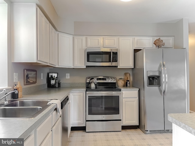 kitchen featuring appliances with stainless steel finishes, white cabinets, light floors, light countertops, and a sink
