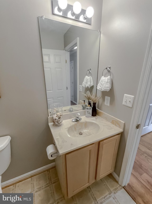 half bathroom with baseboards, vanity, and toilet