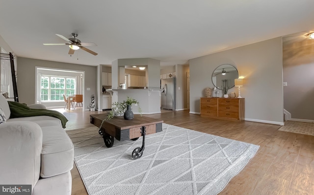 living area with ceiling fan, light wood-style flooring, and baseboards