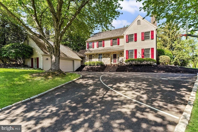 view of front of home with a garage, a front yard, stone siding, a chimney, and stucco siding