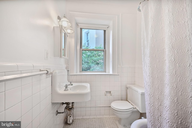 bathroom featuring toilet, wainscoting, tile patterned floors, and tile walls