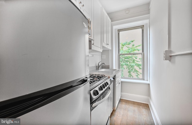 kitchen featuring appliances with stainless steel finishes, a sink, white cabinetry, baseboards, and light wood finished floors