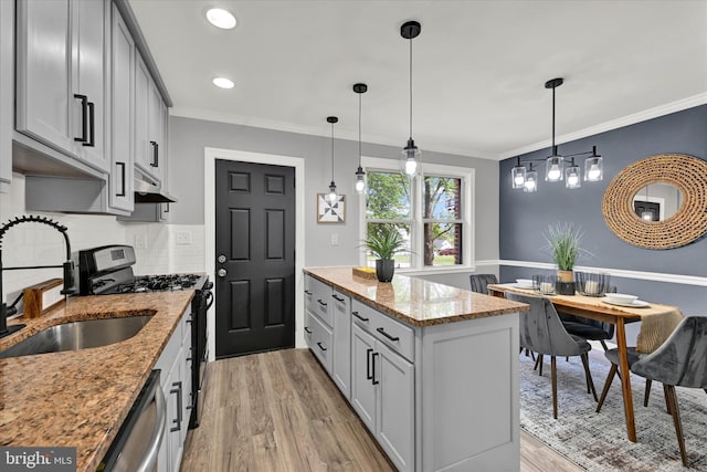 kitchen with appliances with stainless steel finishes, a sink, a center island, light wood-style flooring, and light stone counters