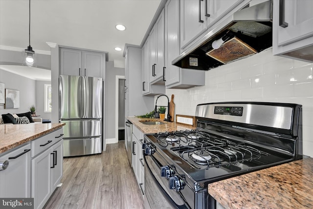 kitchen with appliances with stainless steel finishes, under cabinet range hood, a sink, light stone counters, and tasteful backsplash