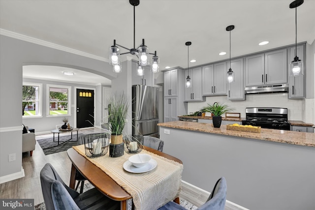 dining area featuring arched walkways, baseboards, wood finished floors, ornamental molding, and recessed lighting