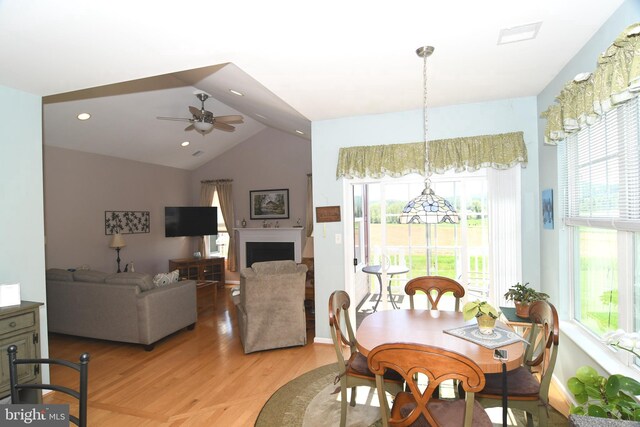 dining room featuring healthy amount of natural light, light wood-style floors, a ceiling fan, lofted ceiling, and a fireplace