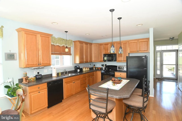 kitchen featuring black appliances, a sink, light wood-style floors, a kitchen breakfast bar, and dark countertops