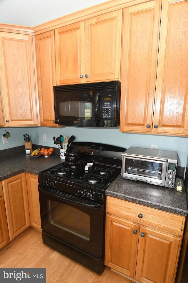 kitchen featuring black appliances, dark countertops, and light wood-style floors