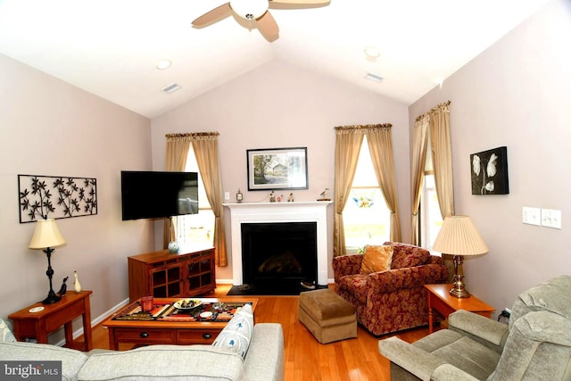 living area featuring wood finished floors, a ceiling fan, vaulted ceiling, and a fireplace with flush hearth